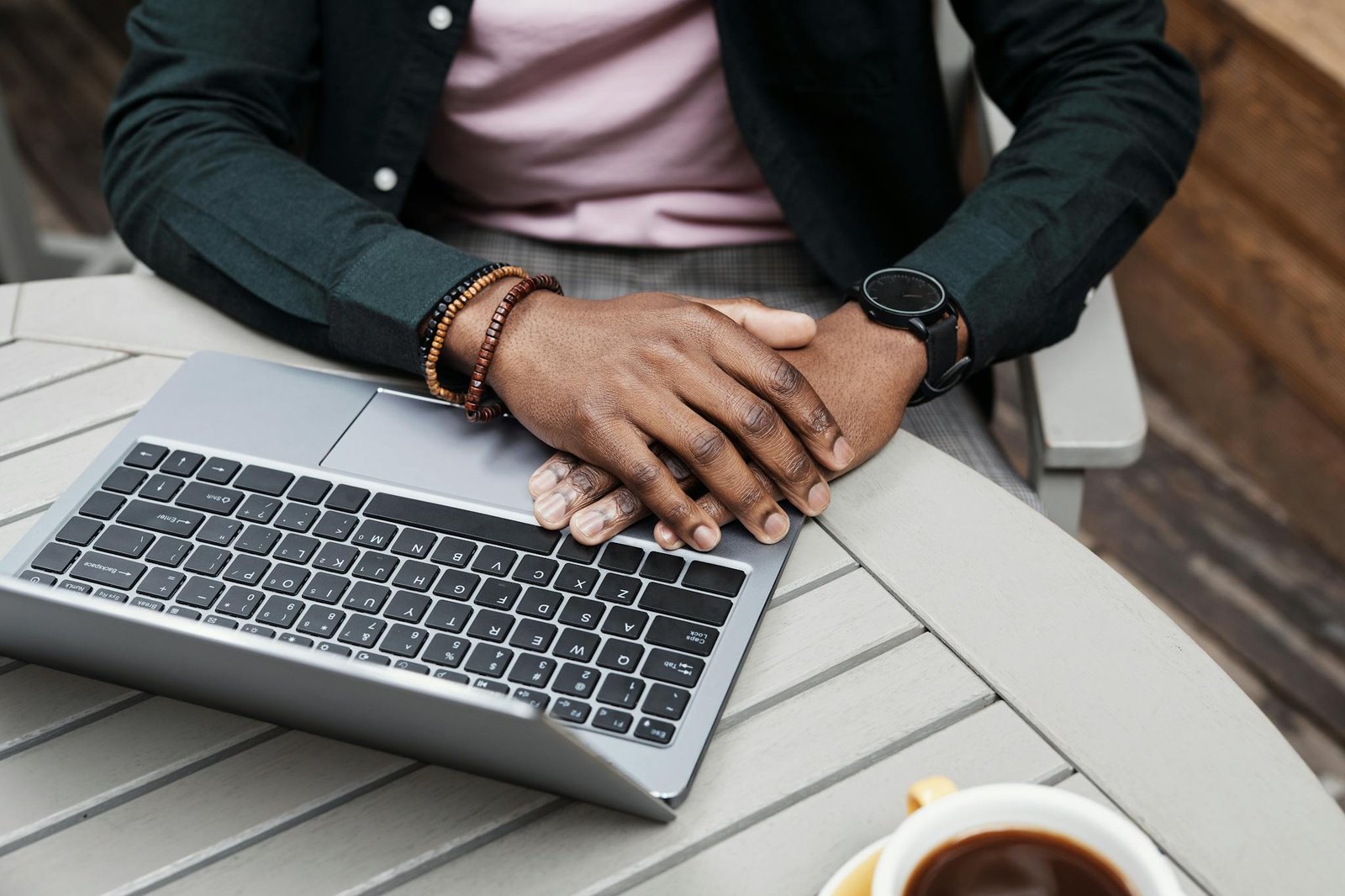A person resting hands on a laptop, outdoors with coffee, suggesting a relaxed work environment.