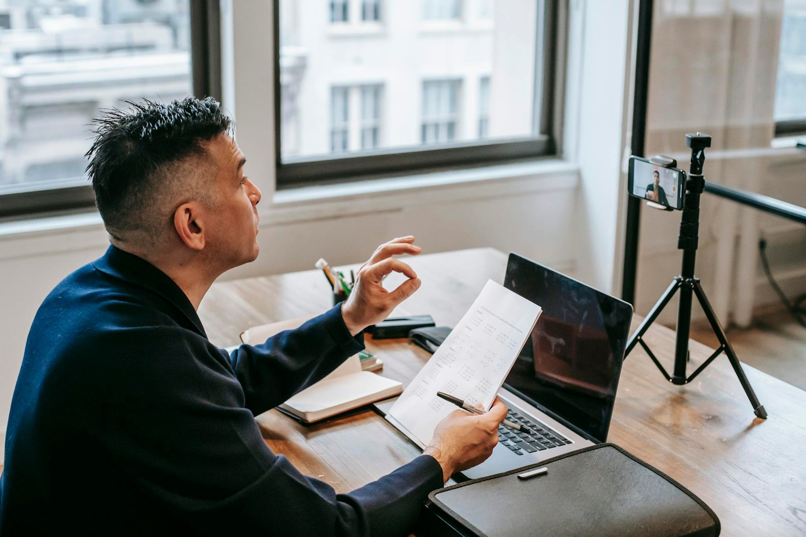 Man using laptop and smartphone for a video call in an office setting.